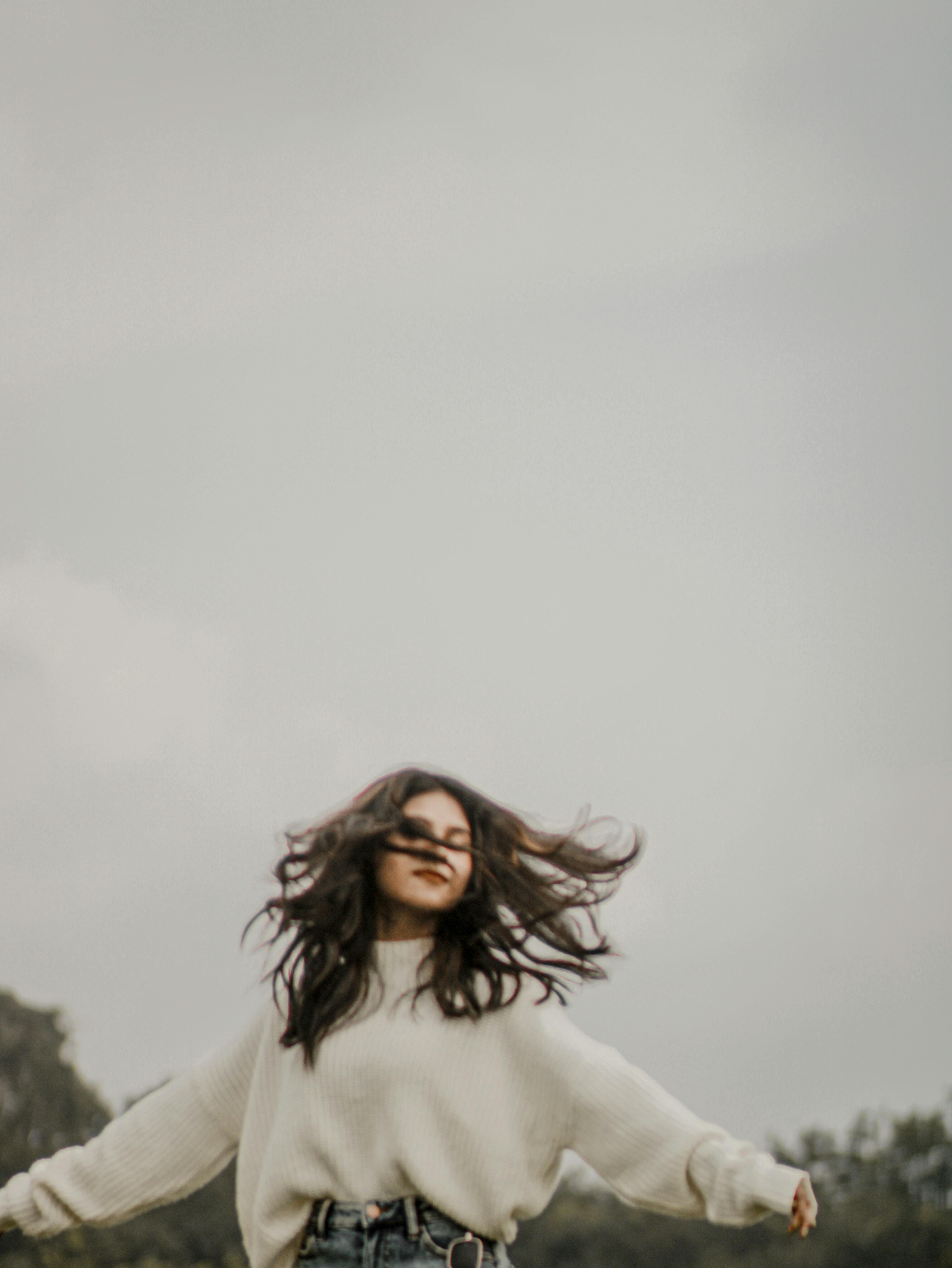 Woman in casual clothing joyfully dancing in an open field, showcasing freedom and happiness.