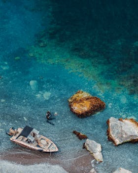 从空中俯瞰，一艘船停泊在岸边，一名潜水员正在清澈的蓝色海水中探索