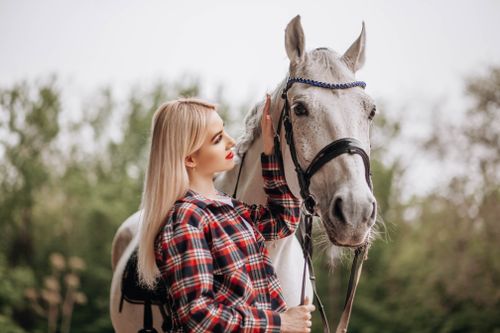 Free A young woman in a plaid shirt gently interacts with a white horse in a natural setting. Stock Photo