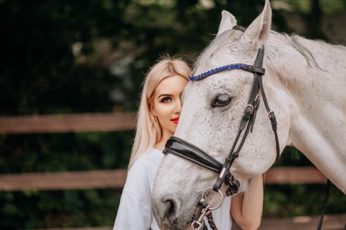 Free Woman poses with a white horse in a serene outdoor setting. Stock Photo