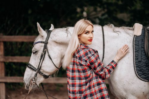 Free Blonde woman in plaid shirt gently petting a white horse outdoors. Stock Photo