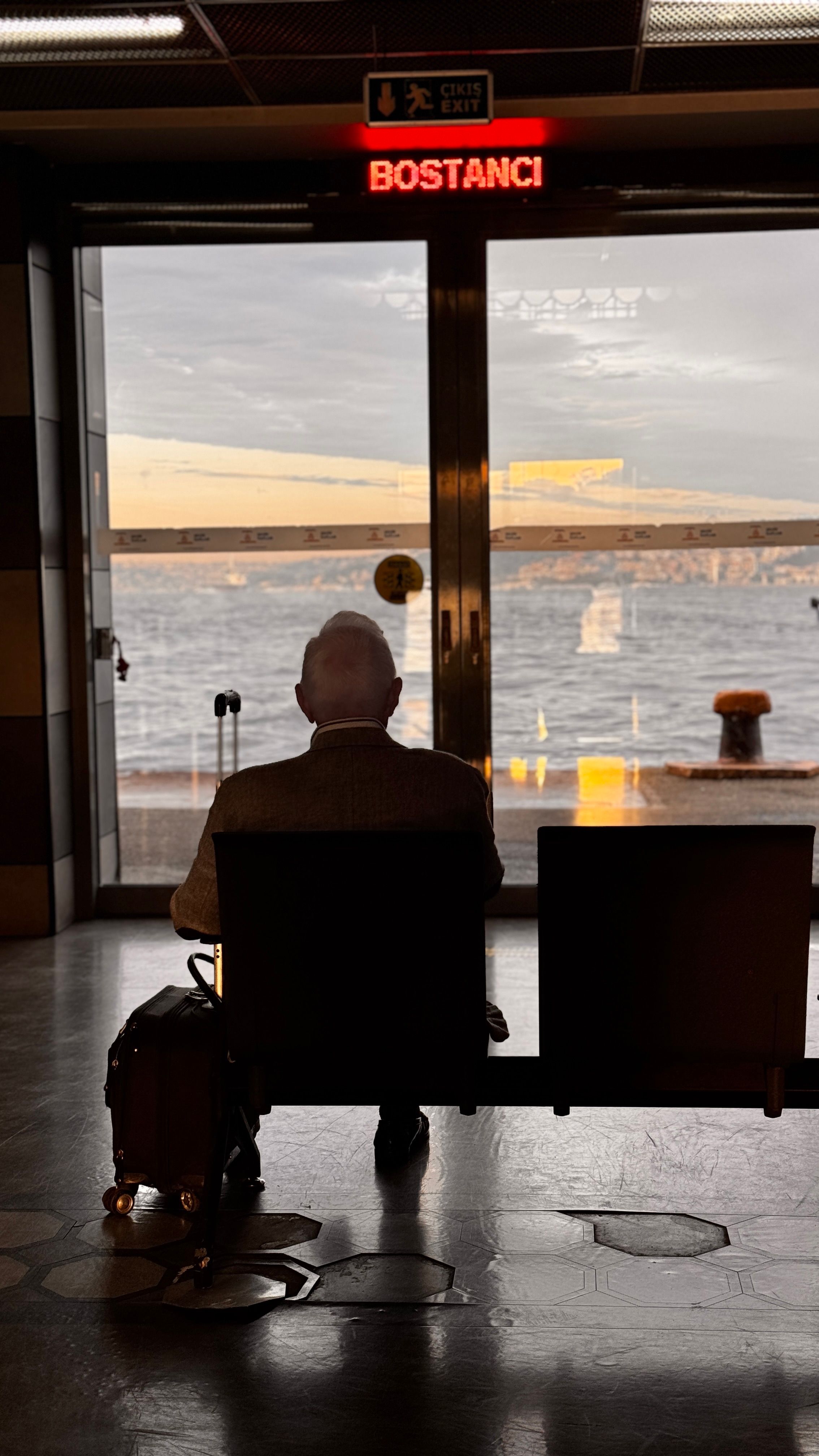 An elderly man sits in Bostancı ferry terminal with a view of the sea, reflecting solitude.