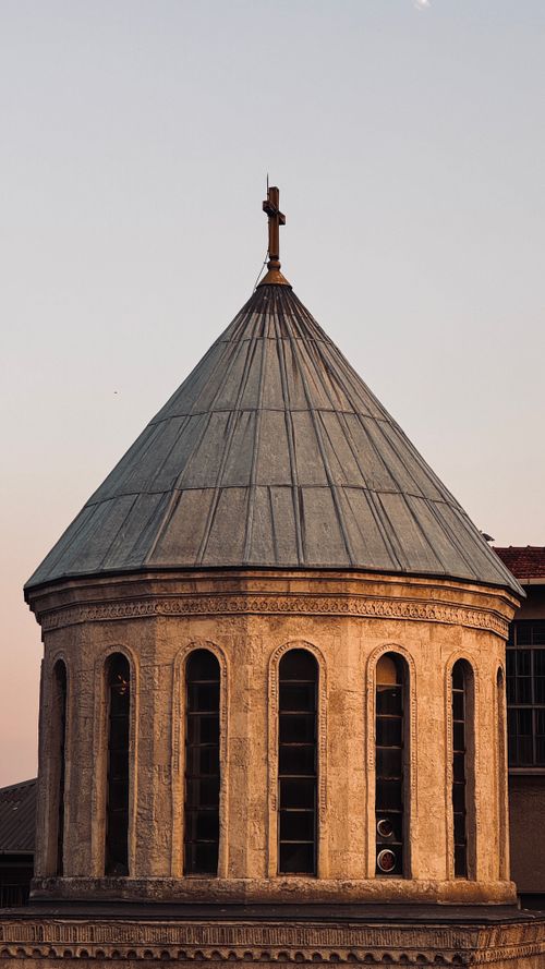 Free Serene view of a historic church dome featuring a cross against a sunset sky. Stock Photo