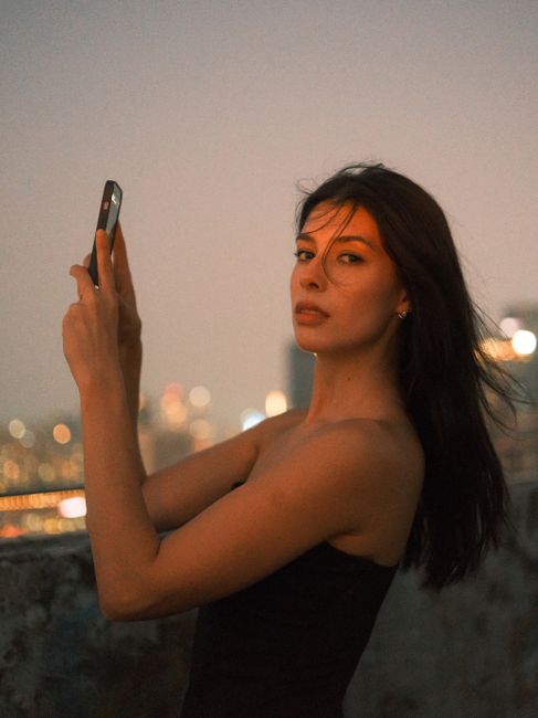 Portrait of a woman capturing the sunset on a rooftop, blending city lights and twilight atmosphere.