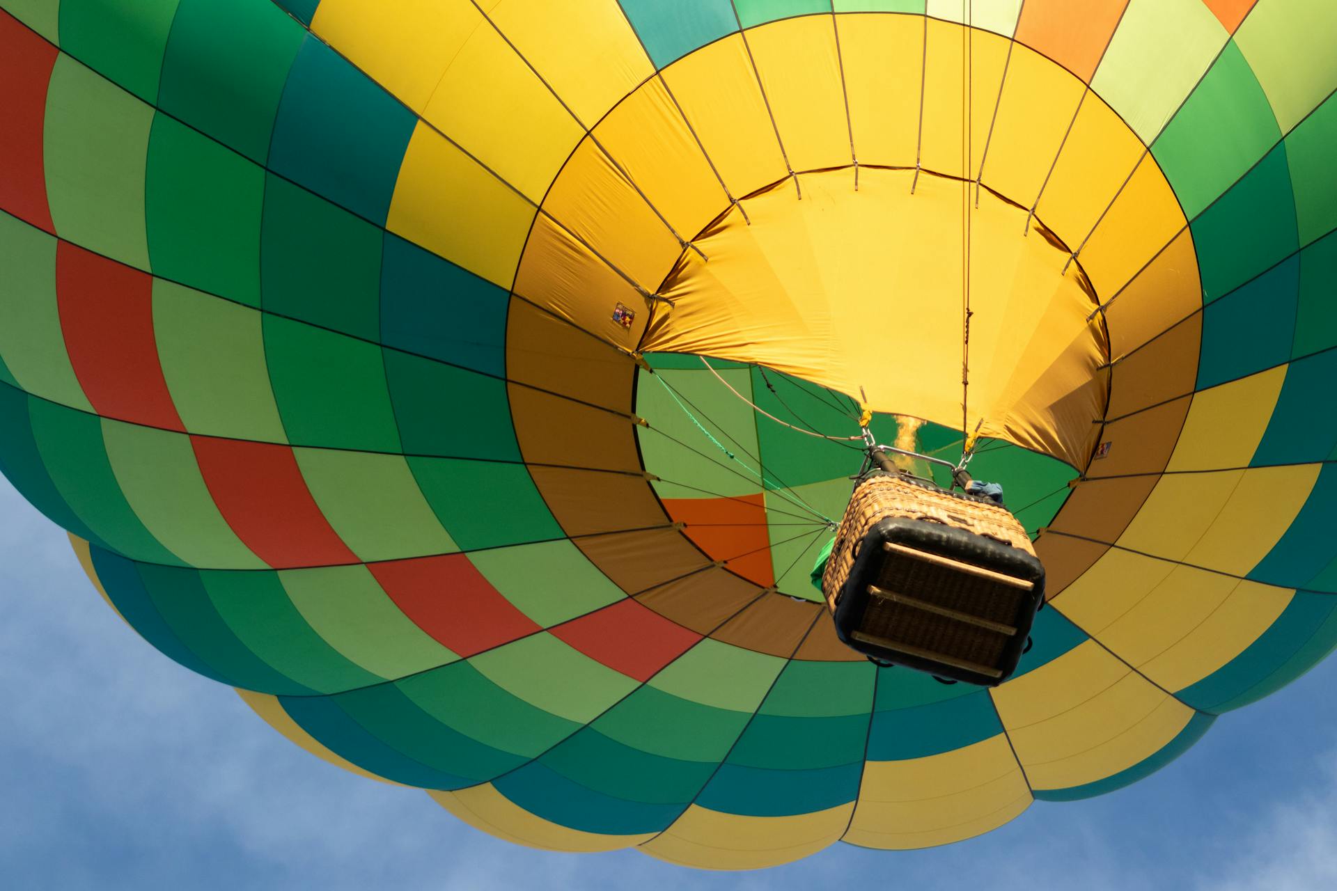 Colorful hot air balloon with basket, viewed from below, soaring in a clear sky.