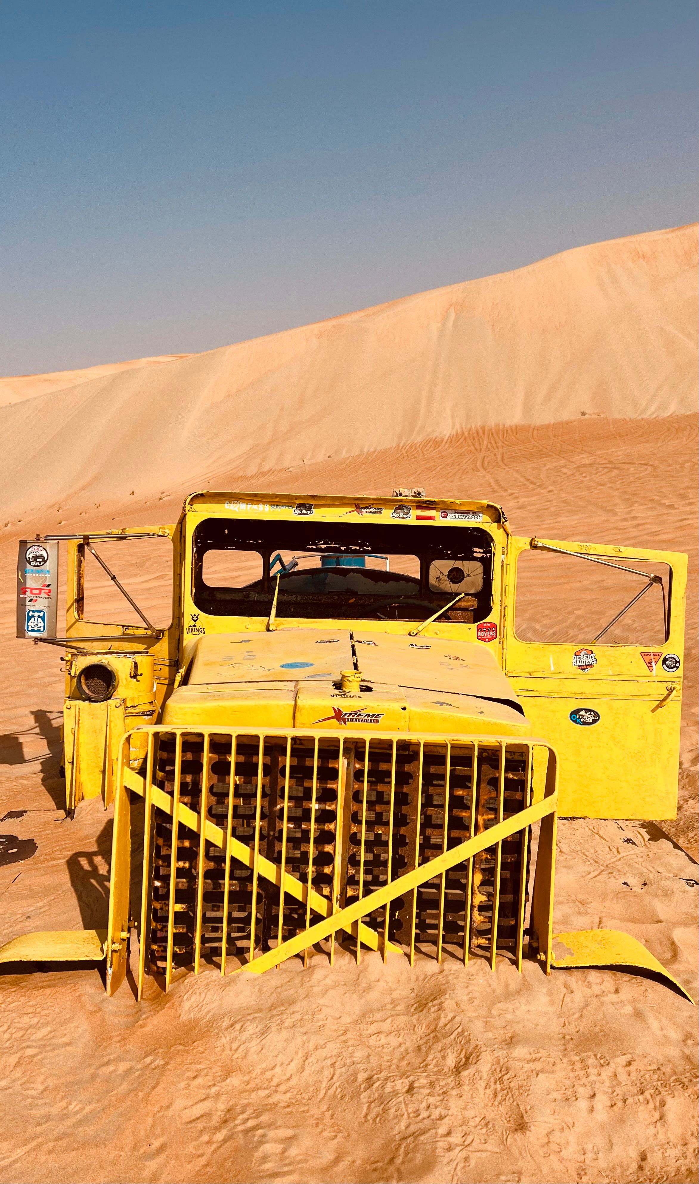 A vibrant yellow vintage truck partially buried in the Abu Dhabi desert sands.