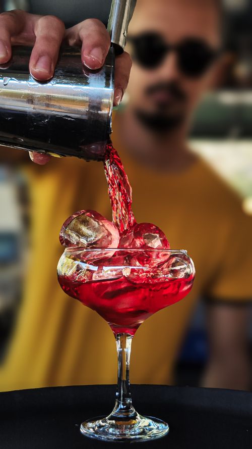 Free A bartender skillfully pours a vibrant red cocktail into a glass filled with ice. Stock Photo