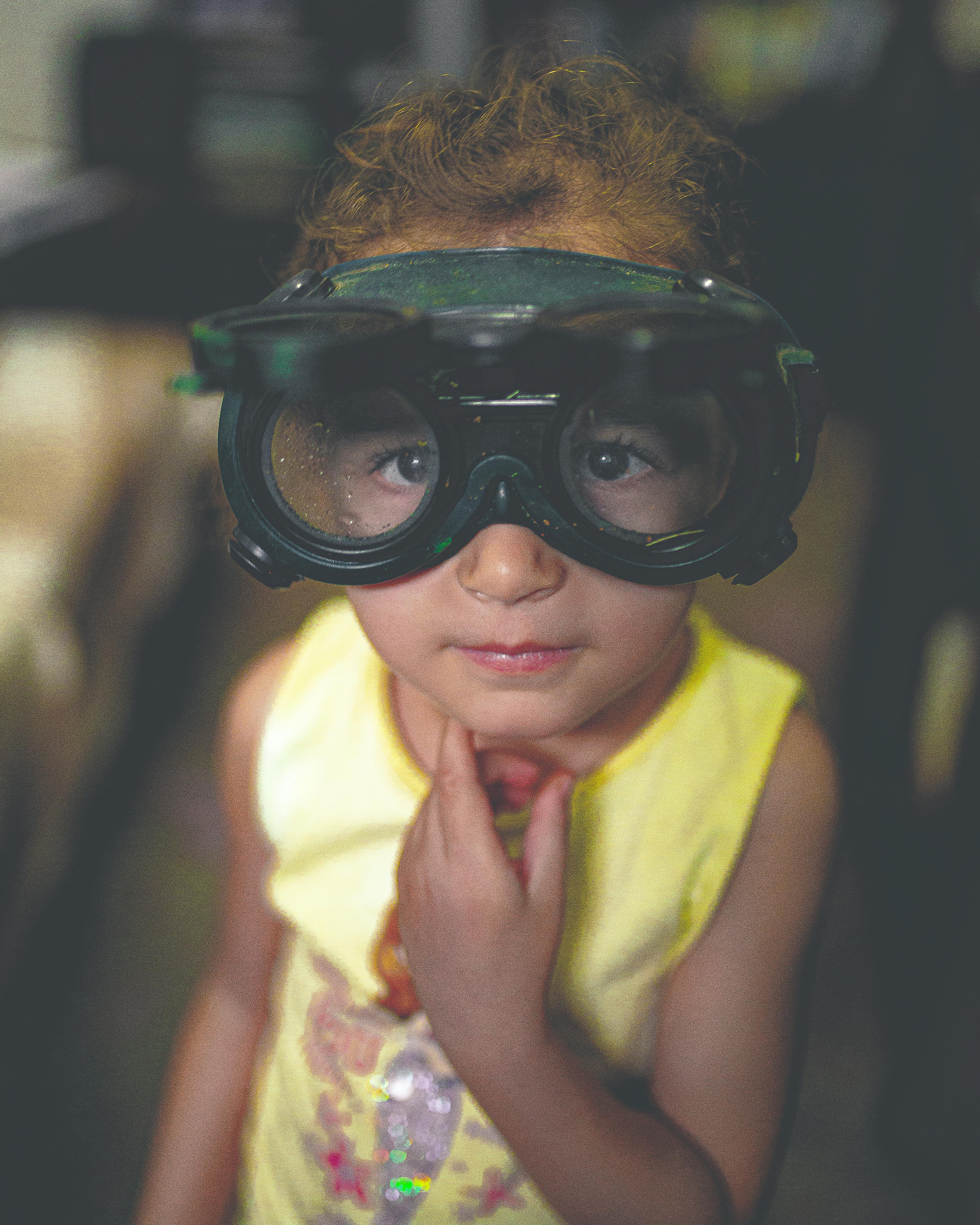 室内，一个戴着超大护目镜的可爱小孩，表情若有所思