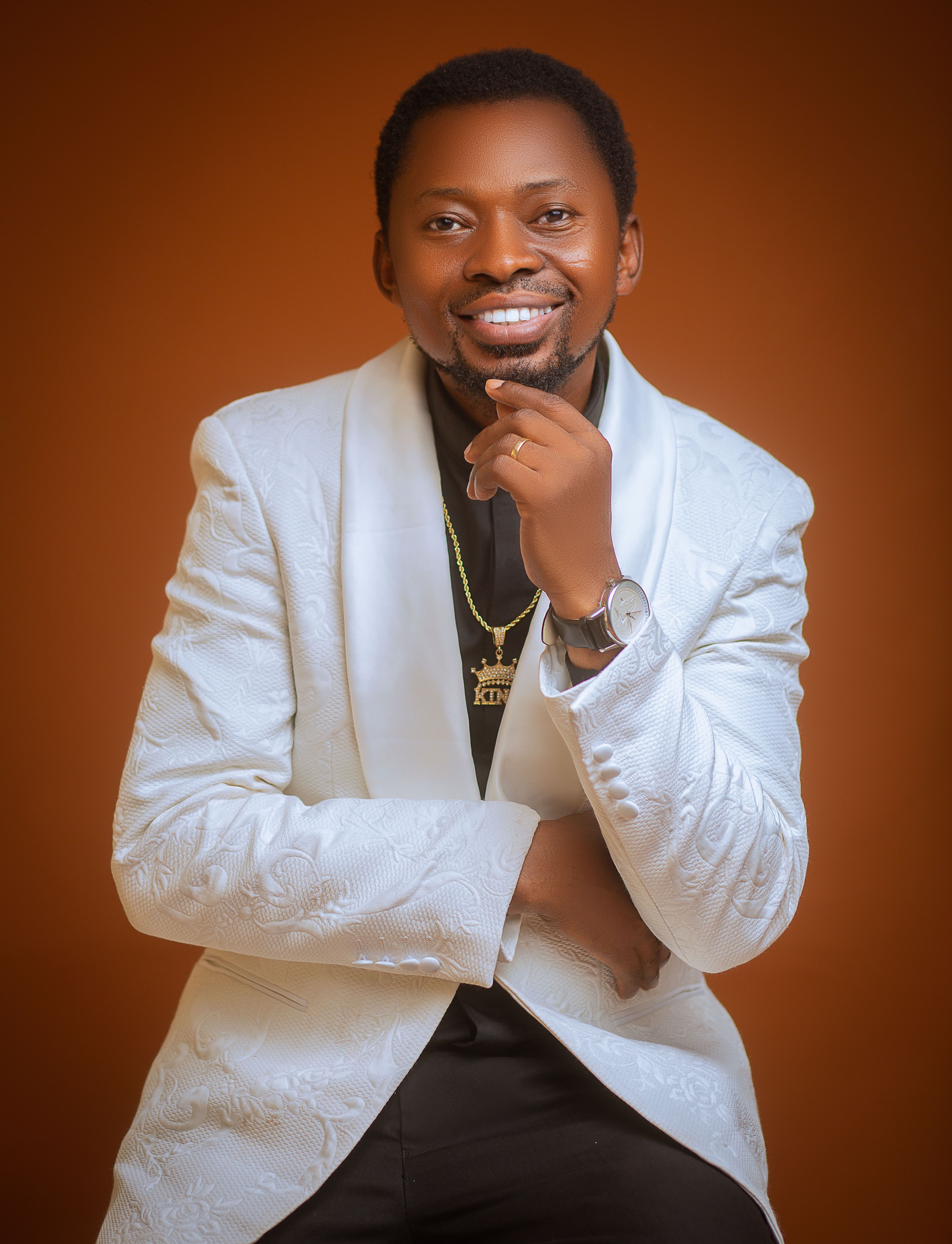 Professional portrait of a smiling man in a white suit on an orange background.