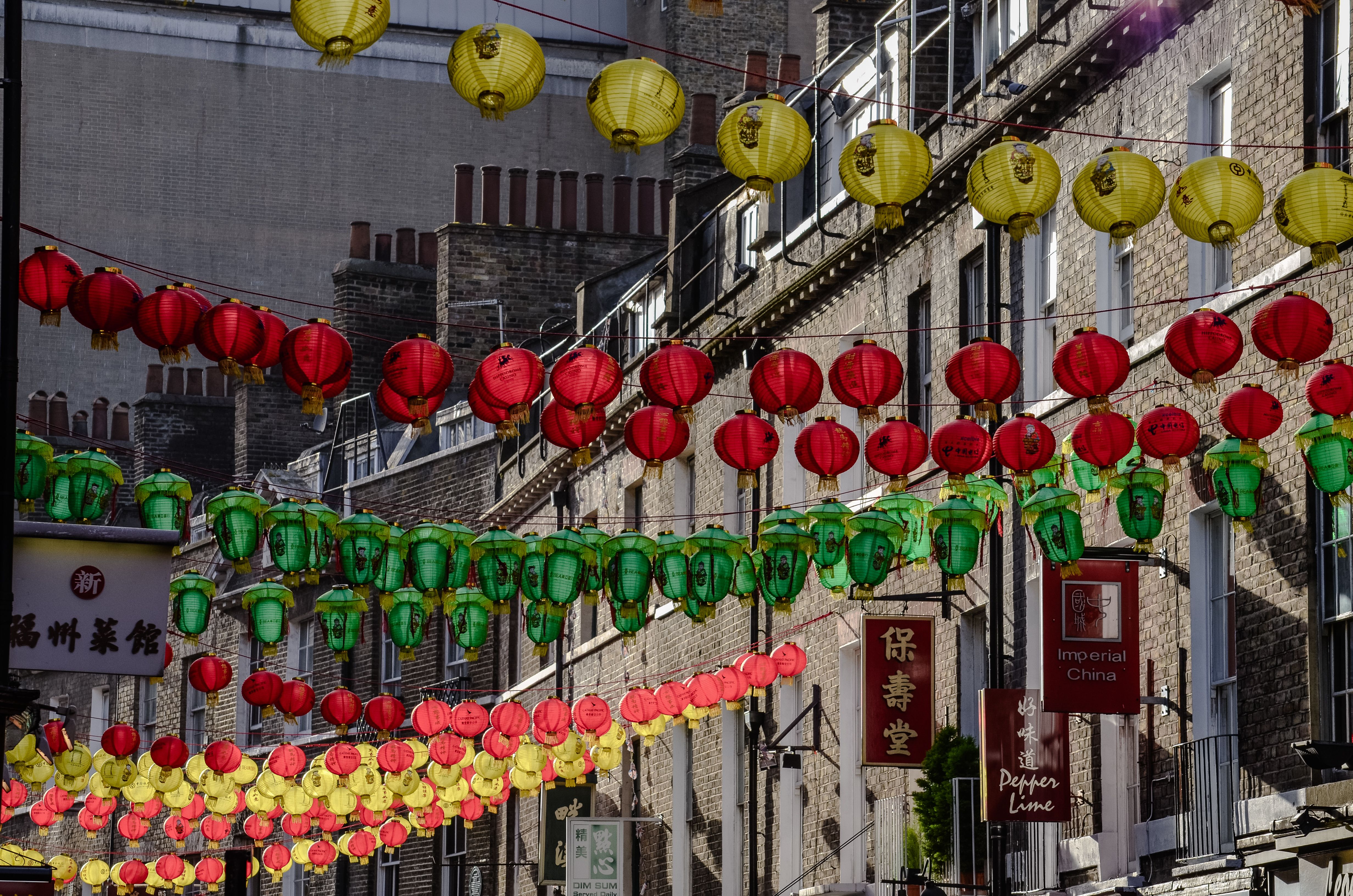Colorful red, green, and yellow lanterns line a bustling street in London's Chinatown, creating a festive atmosphere.