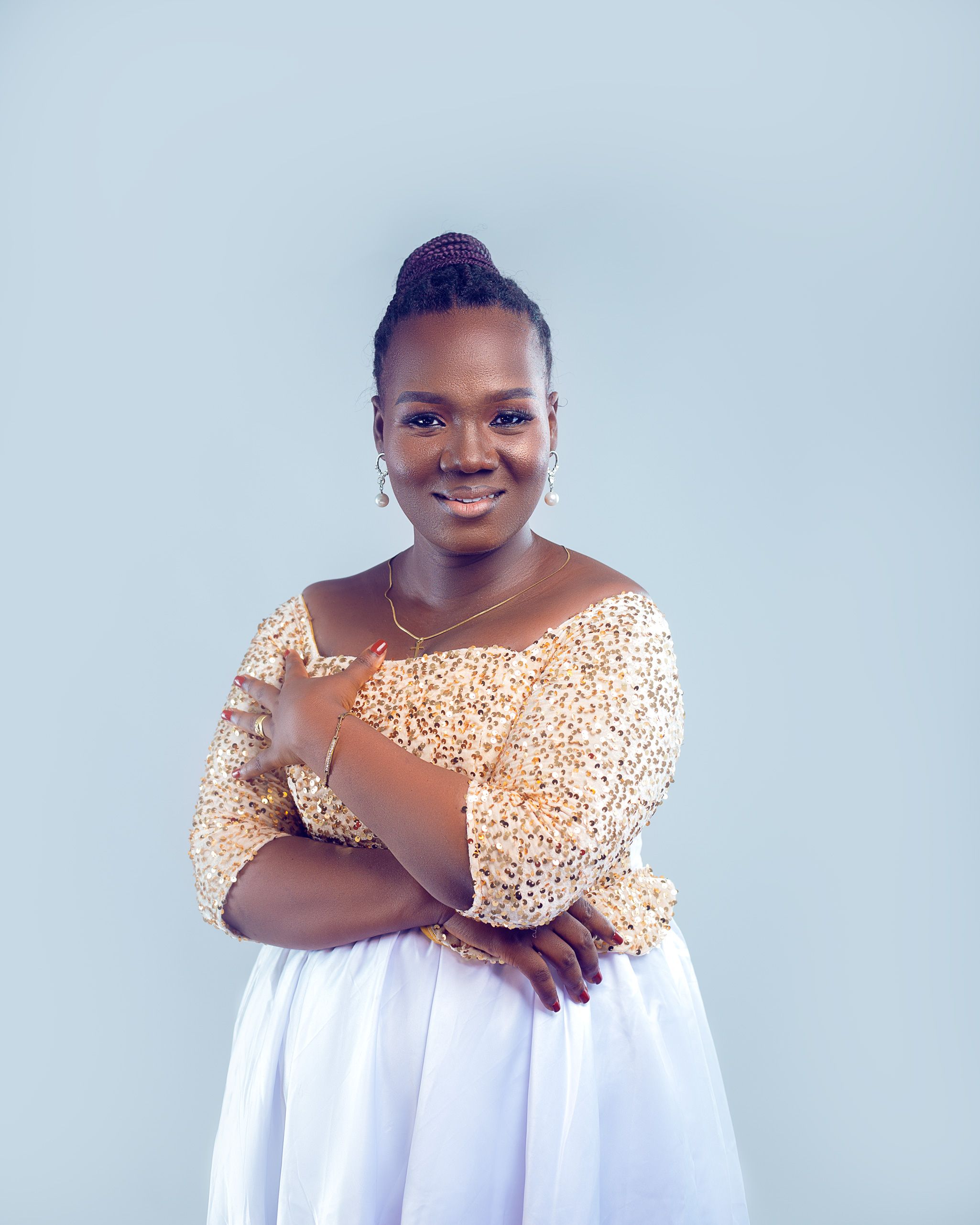 A confident woman in a sparkly gold top and white skirt posing against a light background.