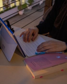 Hands typing on a laptop with a pink notebook and pen on a table.