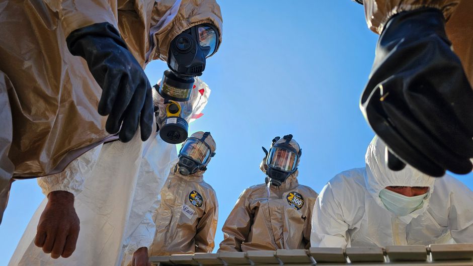 Group of individuals in protective suits and masks working outdoors during the day.