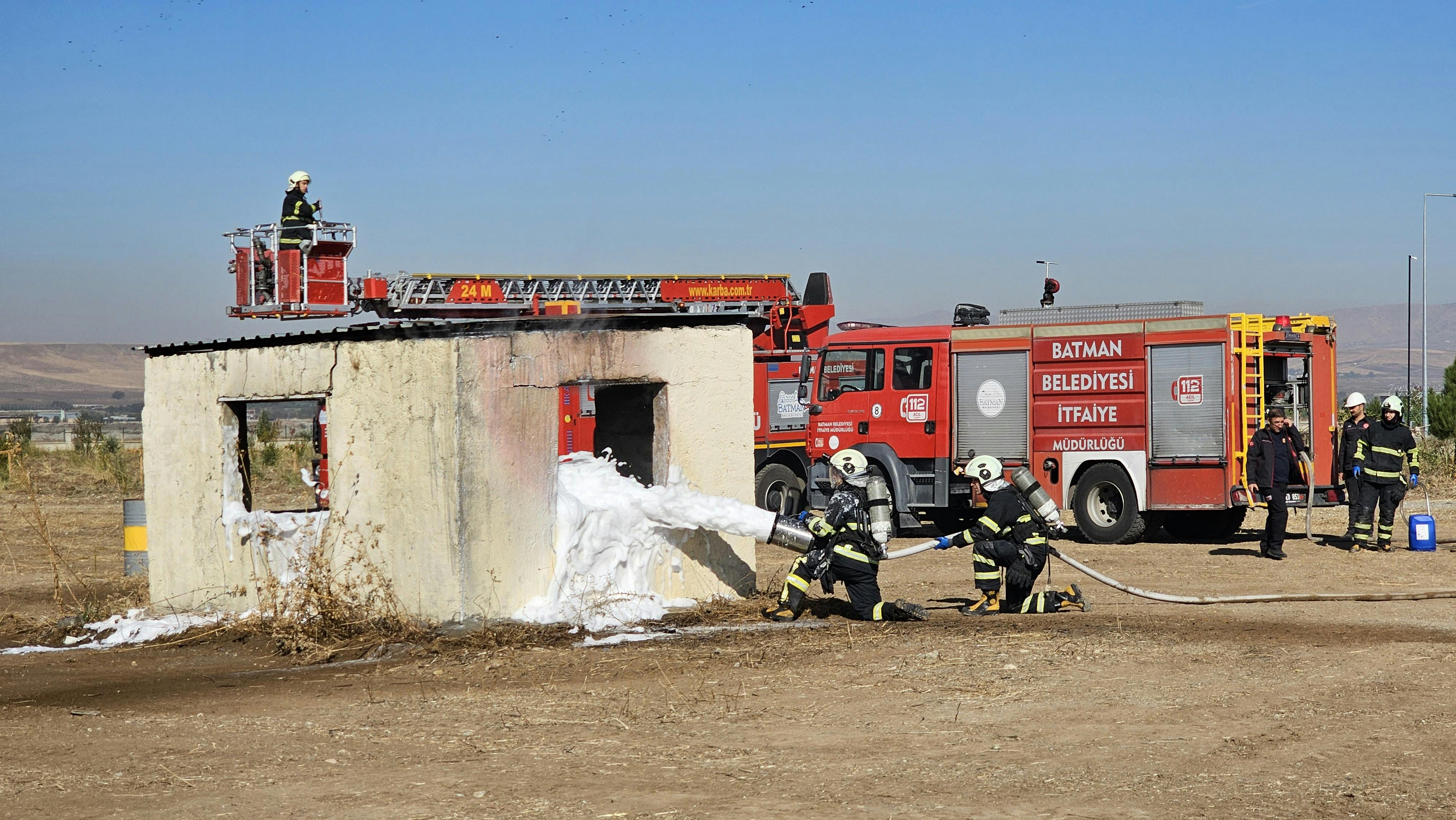 Firefighters conducting safety drill with foam extinguisher and ladder truck outdoors.