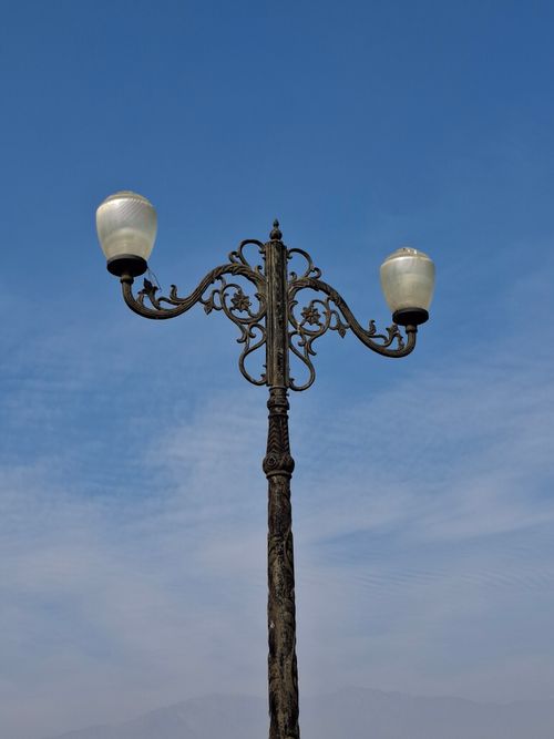 Free Ornate vintage-style street lamp stands alone against a clear blue sky. Ideal for urban aesthetic. Stock Photo