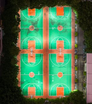 Stunning aerial shot of illuminated basketball courts framed by trees taken at night.