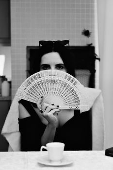 Elegant woman holding a fan in a stylish black and white portrait.
