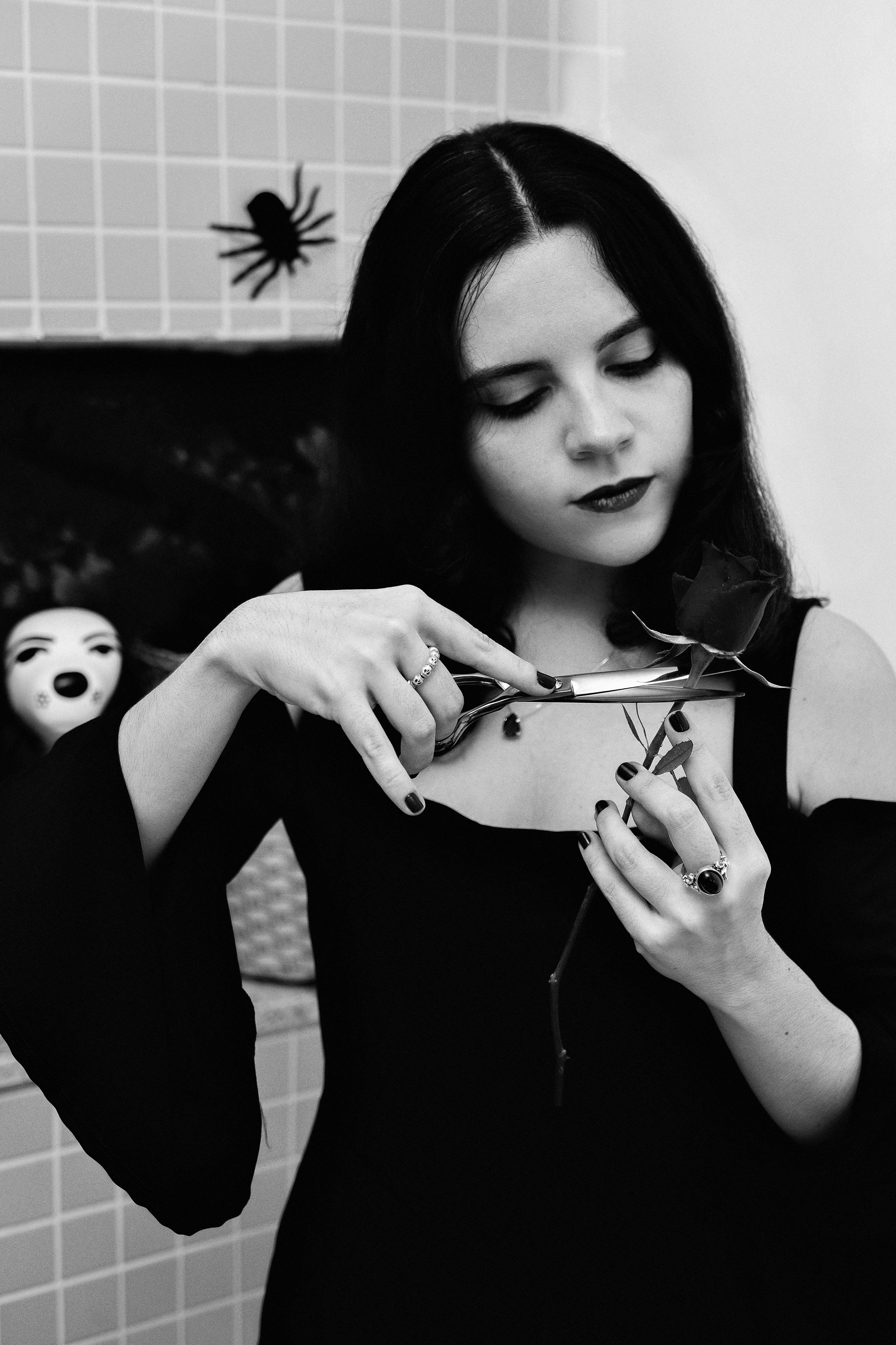 Artistic black and white photo of a Gothic woman cutting a rose with scissors.