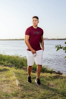 Casually dressed man walking by a scenic riverside during the day, exuding a relaxed vibe.