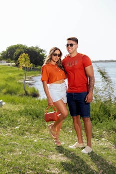 Young couple in casual summer attire smiles by a lakeside on a sunny day.