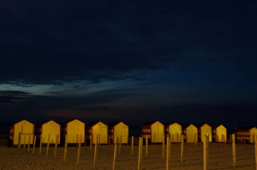 Free Beach cabins illuminated at night with a tranquil sea backdrop and starry sky. Stock Photo