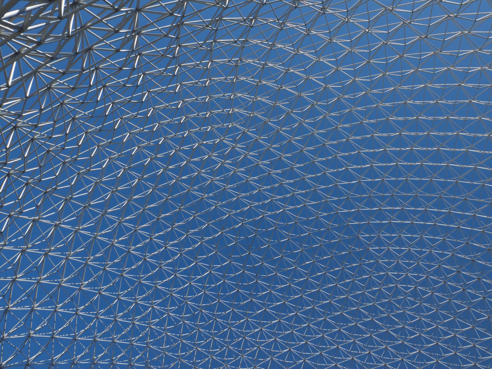Close-up of a modern geodesic dome structure with intricate metal patterns against a clear blue sky.