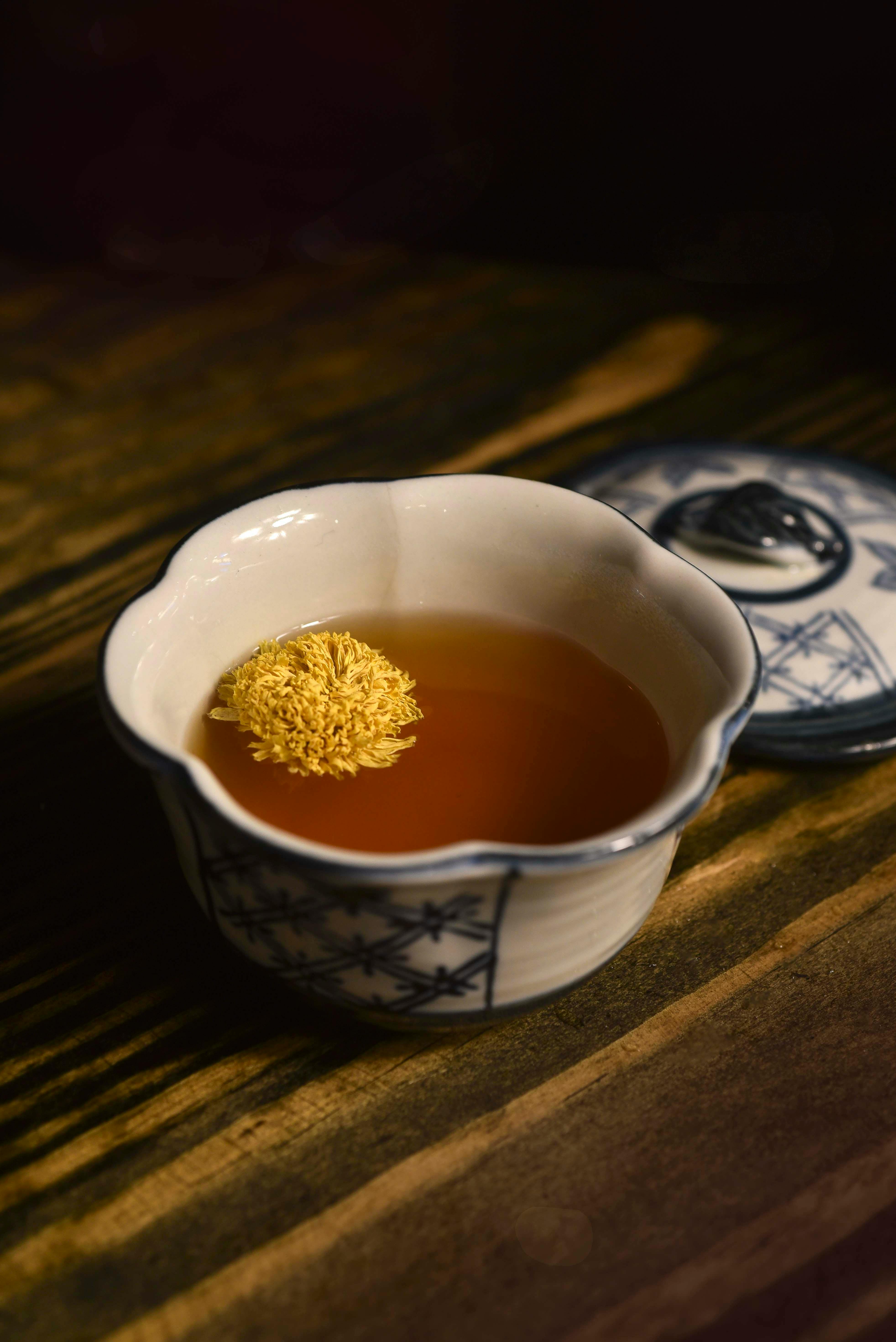 Artistic shot of a steaming tea in a ceramic cup with a chrysanthemum flower.