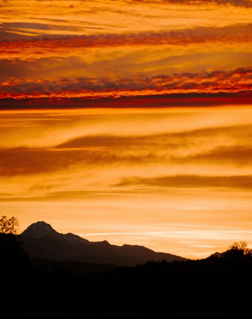 A breathtaking mountain silhouette under a fiery orange sunset sky.