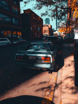 A classic Toyota MR2 parked on a city street, surrounded by autumn leaves and architecture.