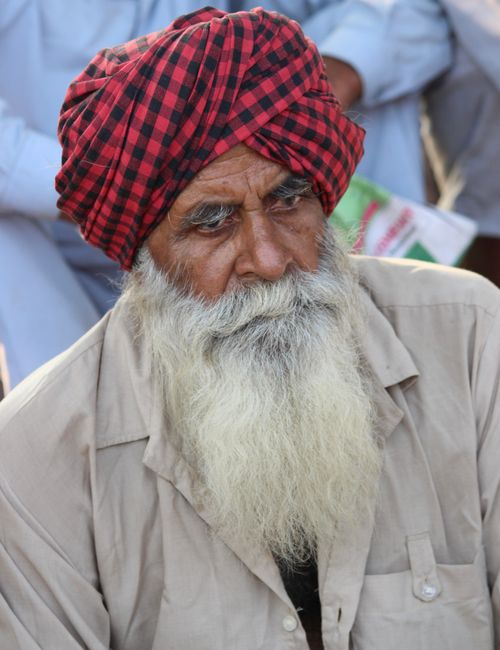 Free Portrait of an elderly man with a red plaid turban, deep in thought outdoors. Stock Photo