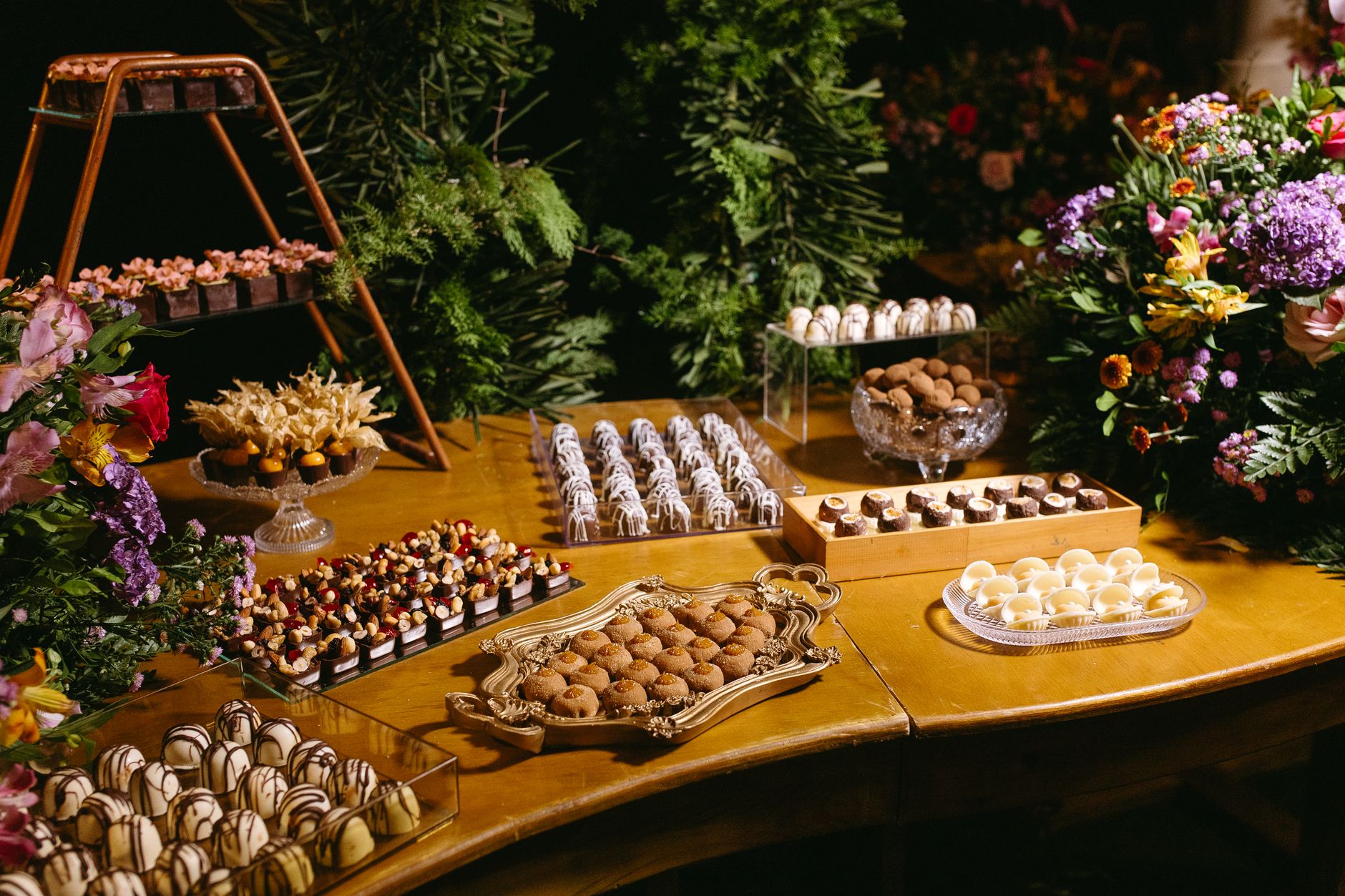 A beautifully arranged dessert table featuring assorted chocolates and pastries, surrounded by floral decorations.