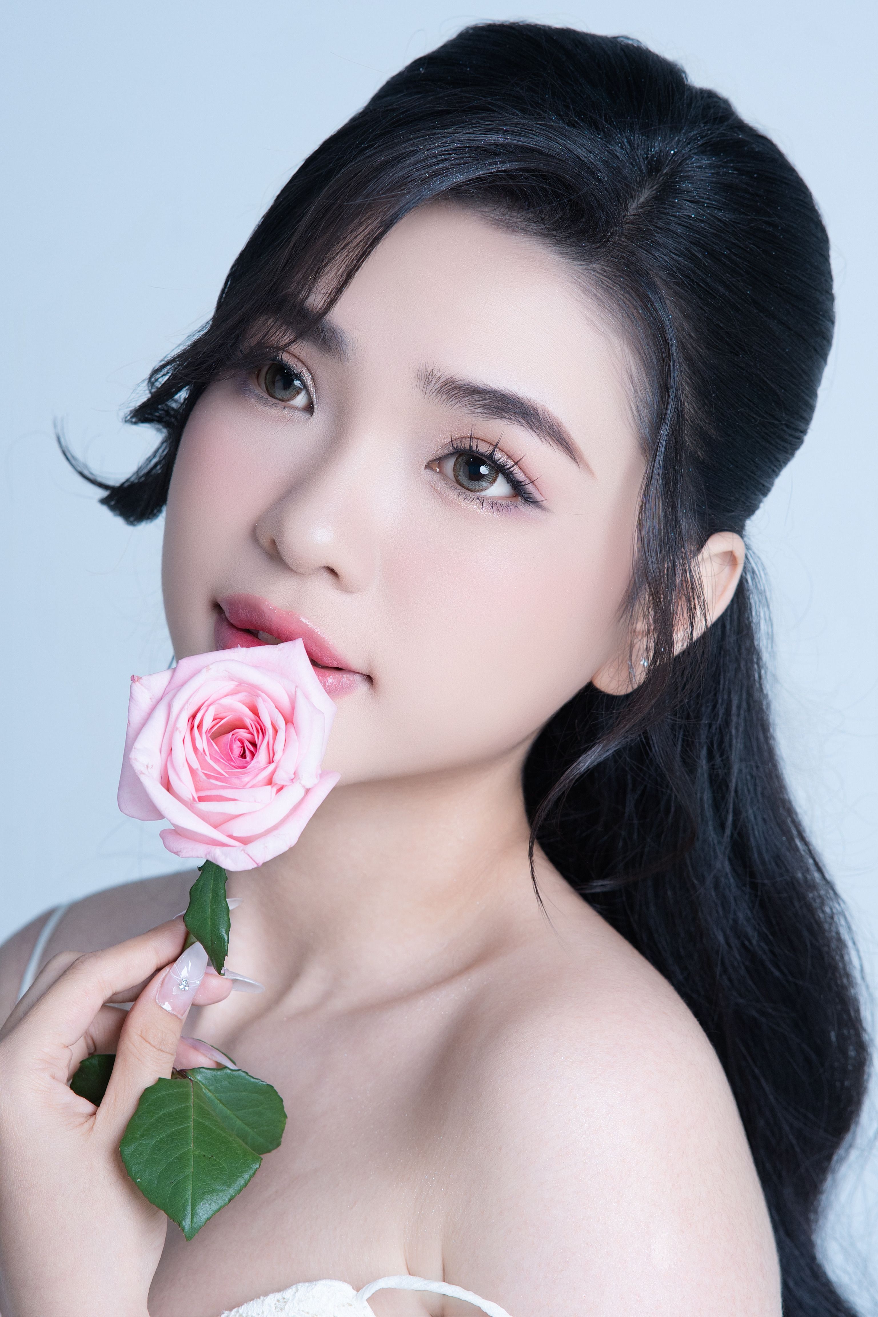 Graceful portrait of a woman gently holding a pink rose with a serene expression.