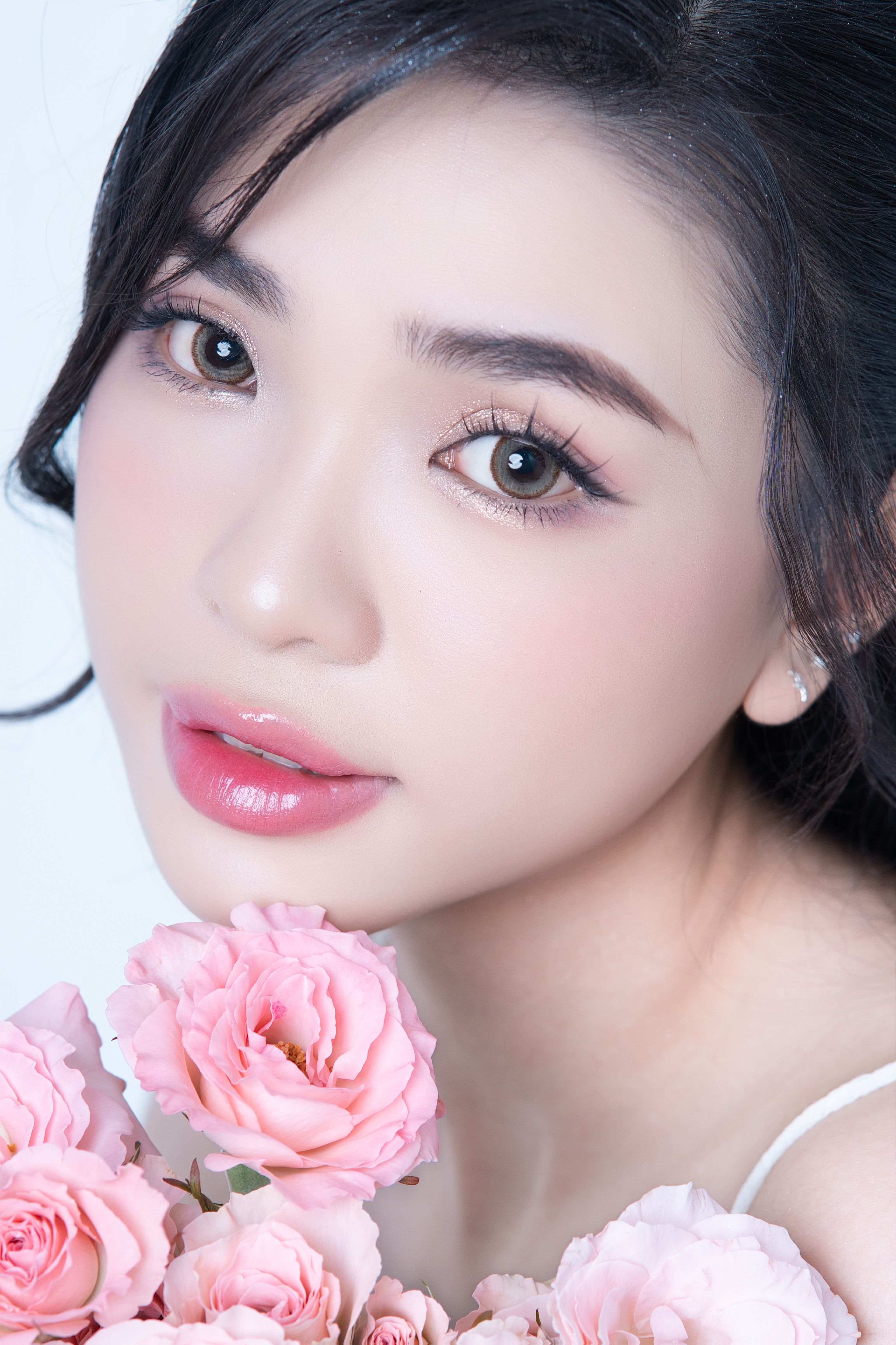 Close-up of a woman with gentle makeup and pink roses, evoking freshness and beauty.
