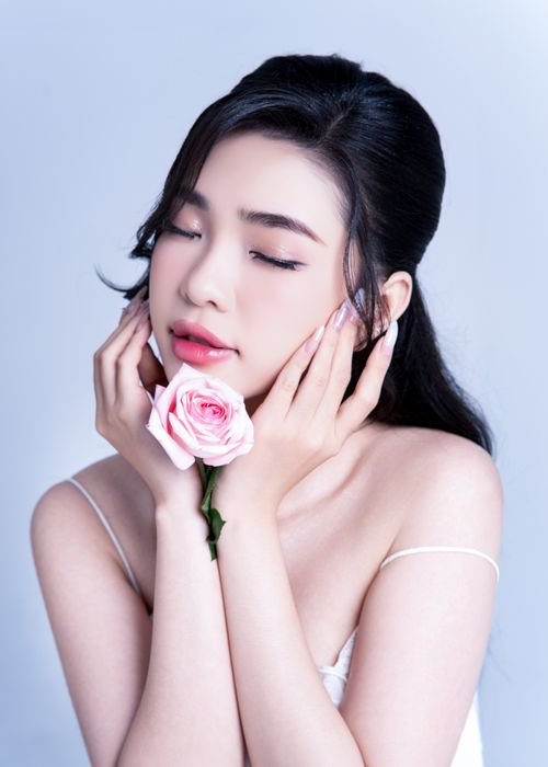 Free Serene portrait of a woman gently holding a pink rose, expressing elegance and beauty. Stock Photo