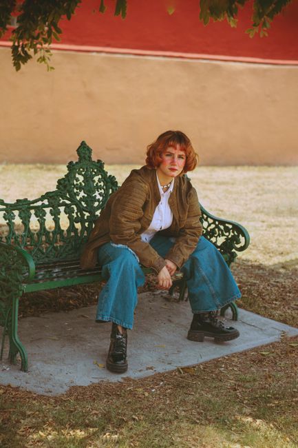 Fotomural Una joven mujer se sienta en un banco verde ornamentado en un entorno de parque, mostrando un estilo casual.