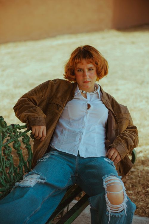 Free Casual portrait of a young woman with red hair wearing casual attire sitting on an outdoor bench. Stock Photo