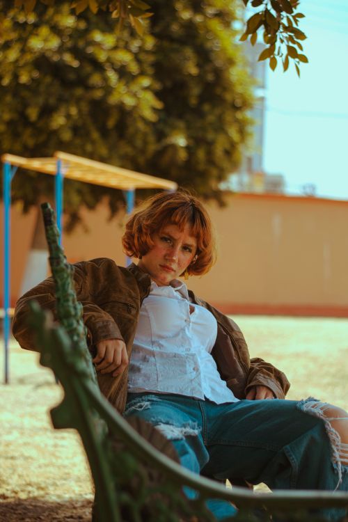 Free Casual fashion portrait of a young adult relaxing on a park bench in natural lighting. Stock Photo