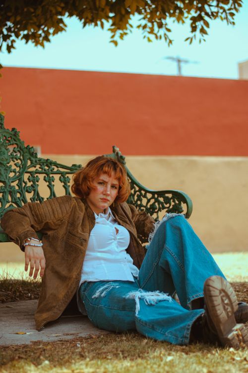 Free Relaxed woman sitting on a vintage bench outdoors, embodying a casual and rustic style. Stock Photo