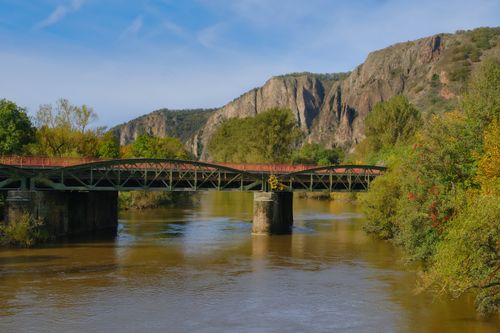 Free A scenic view of a river bridge surrounded by rocky mountains and lush greenery. Stock Photo