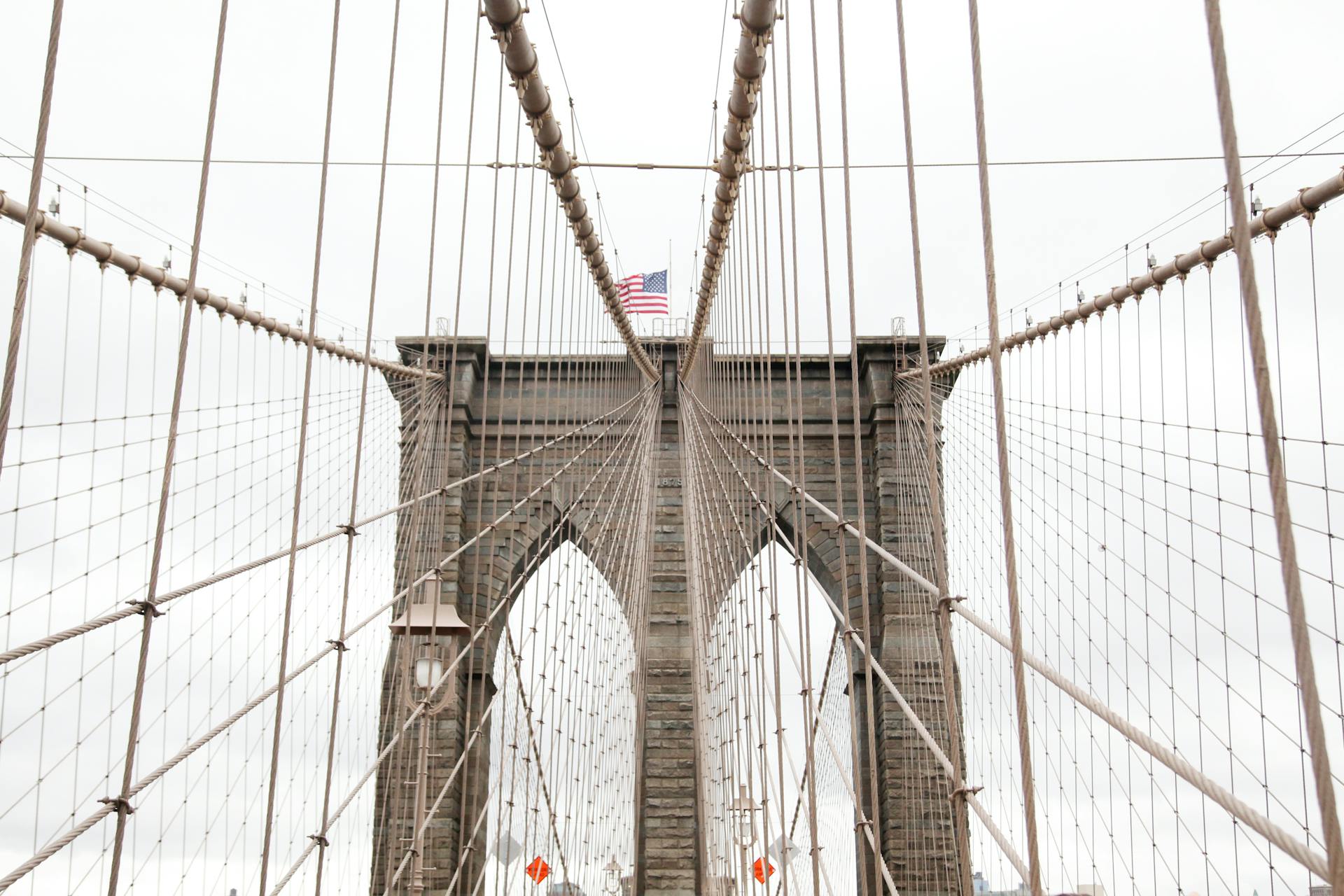 Symmetrical view of Brooklyn Bridge cables with American flag in New York City.