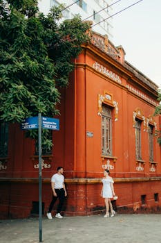 A couple walks by a vivid red historic building in an urban setting.