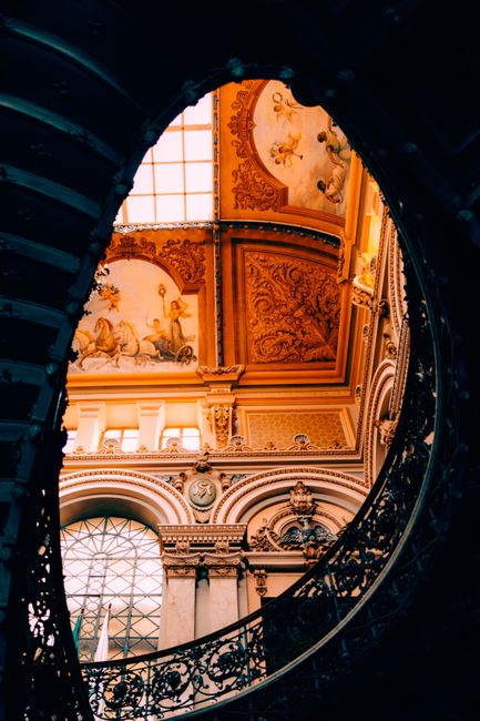 Baroque ceiling and art in an ornate architectural setting viewed through a circular stairwell.