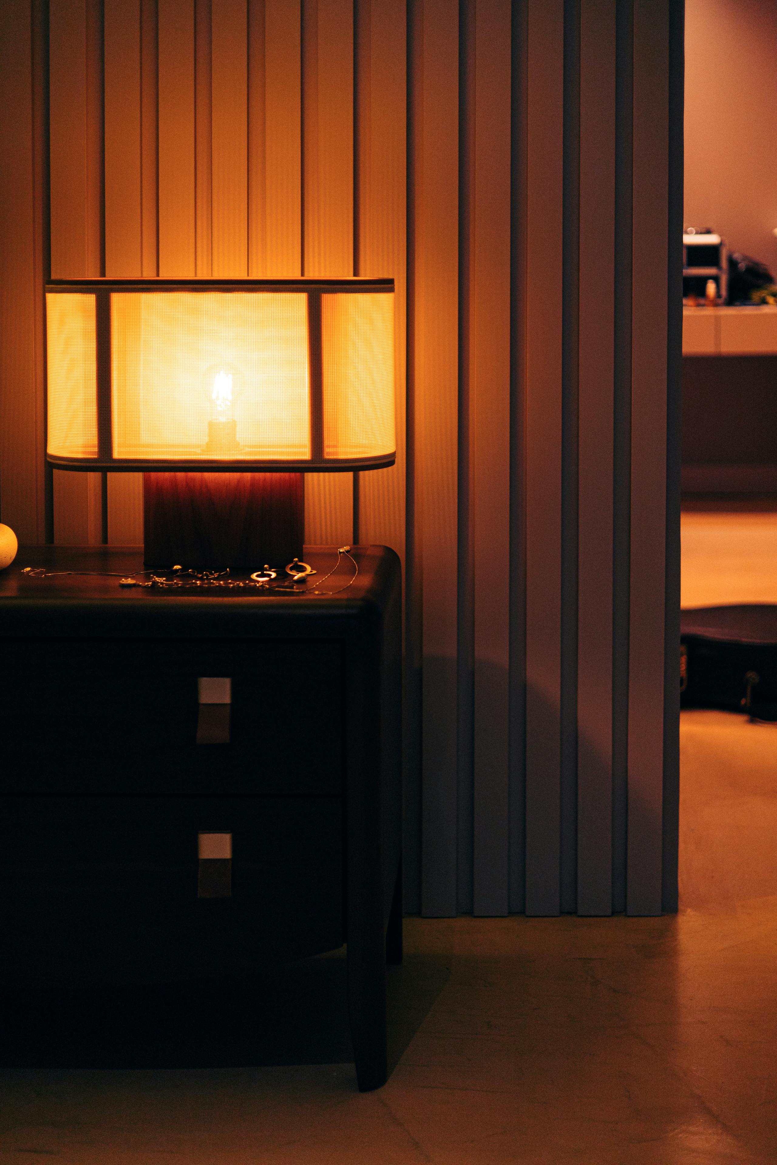 Cozy room with warm lamp glow on a wooden nightstand, perfect for serene ambiance.
