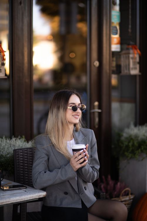 Free Stylish woman enjoying coffee at outdoor cafe, exuding relaxed urban vibe. Stock Photo