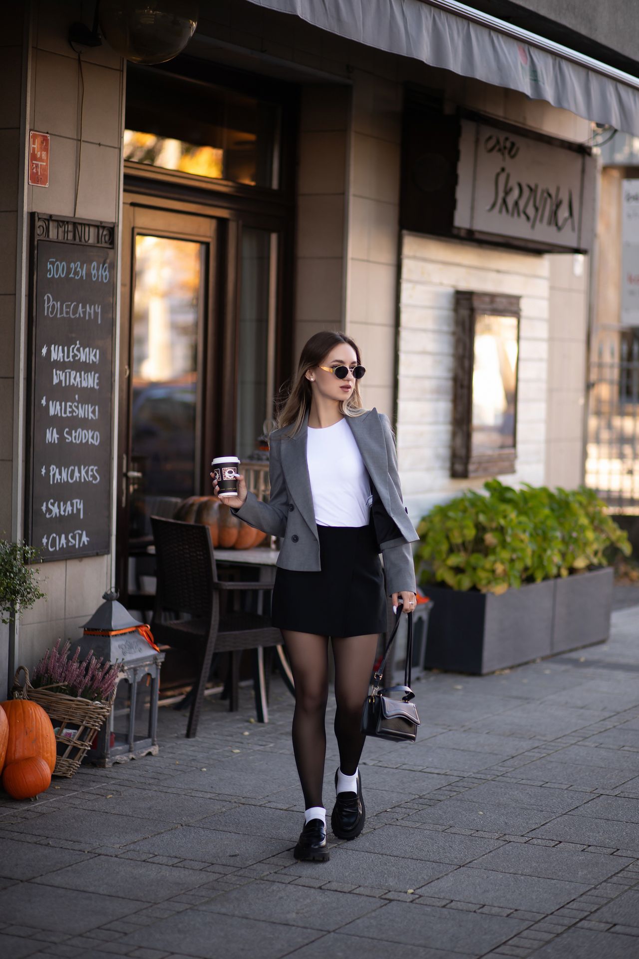 Woman in a gray blazer layered over a white tee and black skirt outside a cafe