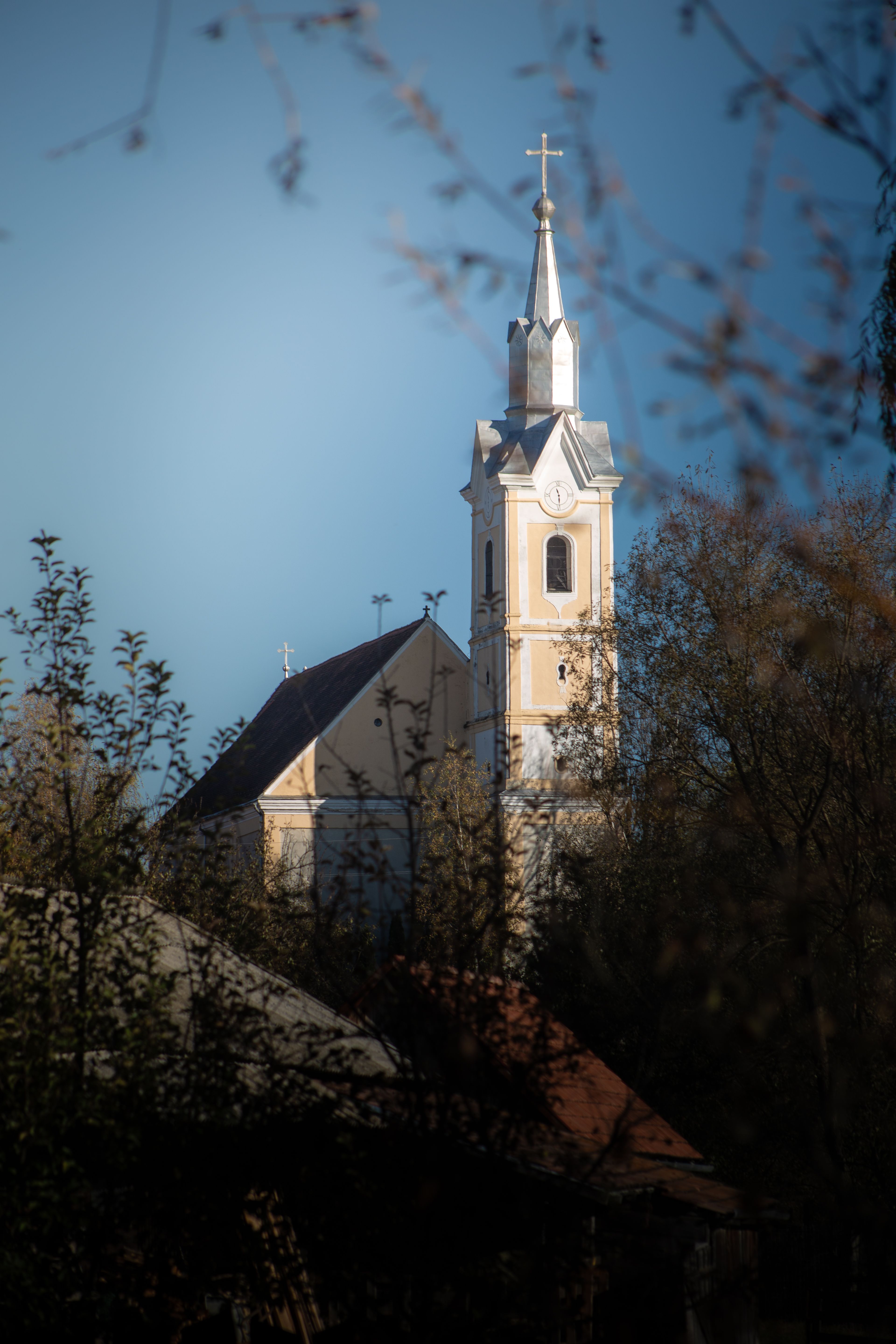 A picturesque view of a historic church tower surrounded by foliage on a sunny day.