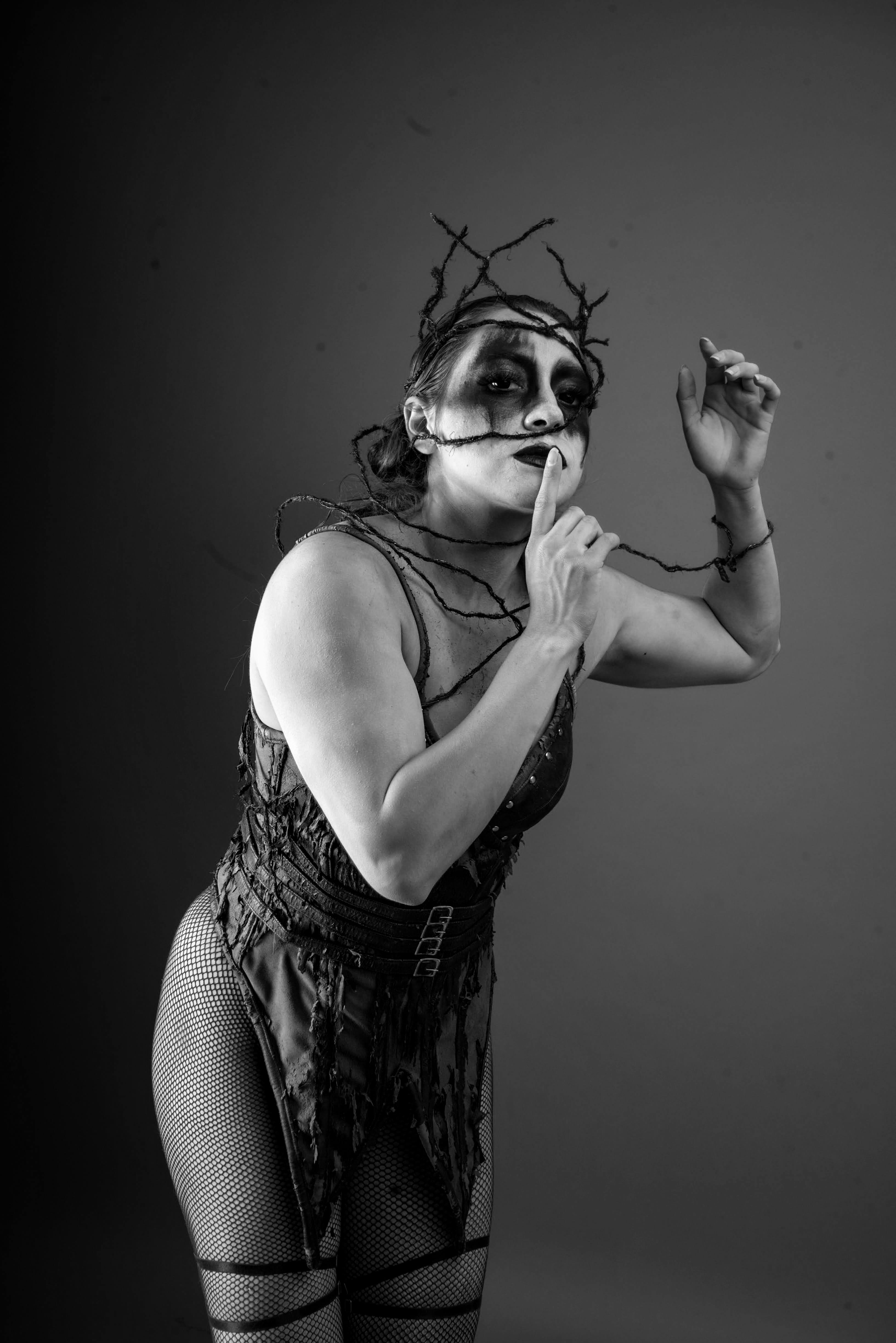 A striking black and white portrait of a person in gothic costume with dramatic makeup and facial expression.
