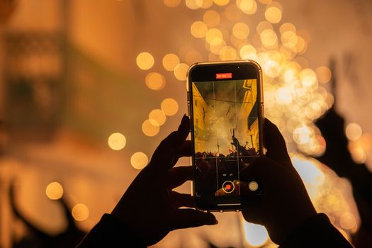 A person records a vibrant fireworks display using a smartphone at night.