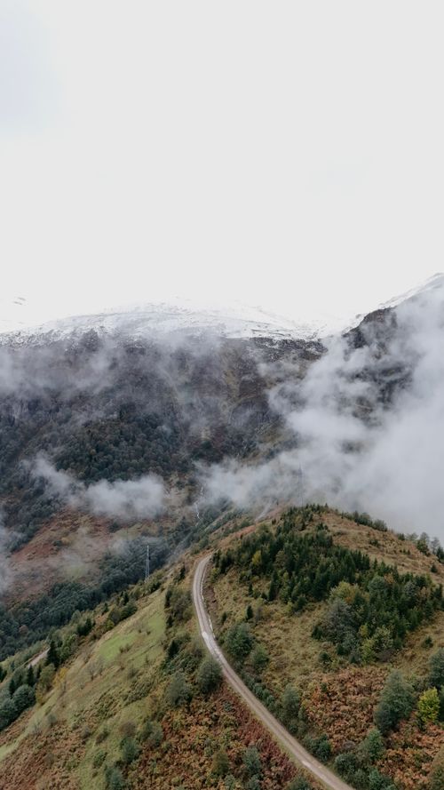 Free A winding road through misty mountains with lush greenery and distant snow-capped peaks. Stock Photo