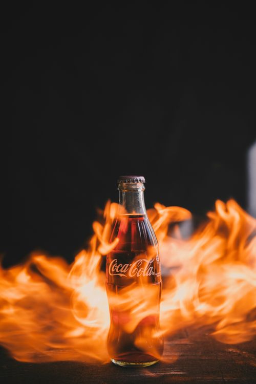 Free Dramatic image of a Coca-Cola bottle amidst vibrant flames, creating a bold and fiery effect. Stock Photo